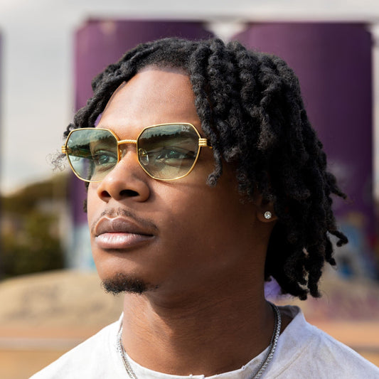 Man wearing green-tinted sunglasses and a white shirt with text, outdoors