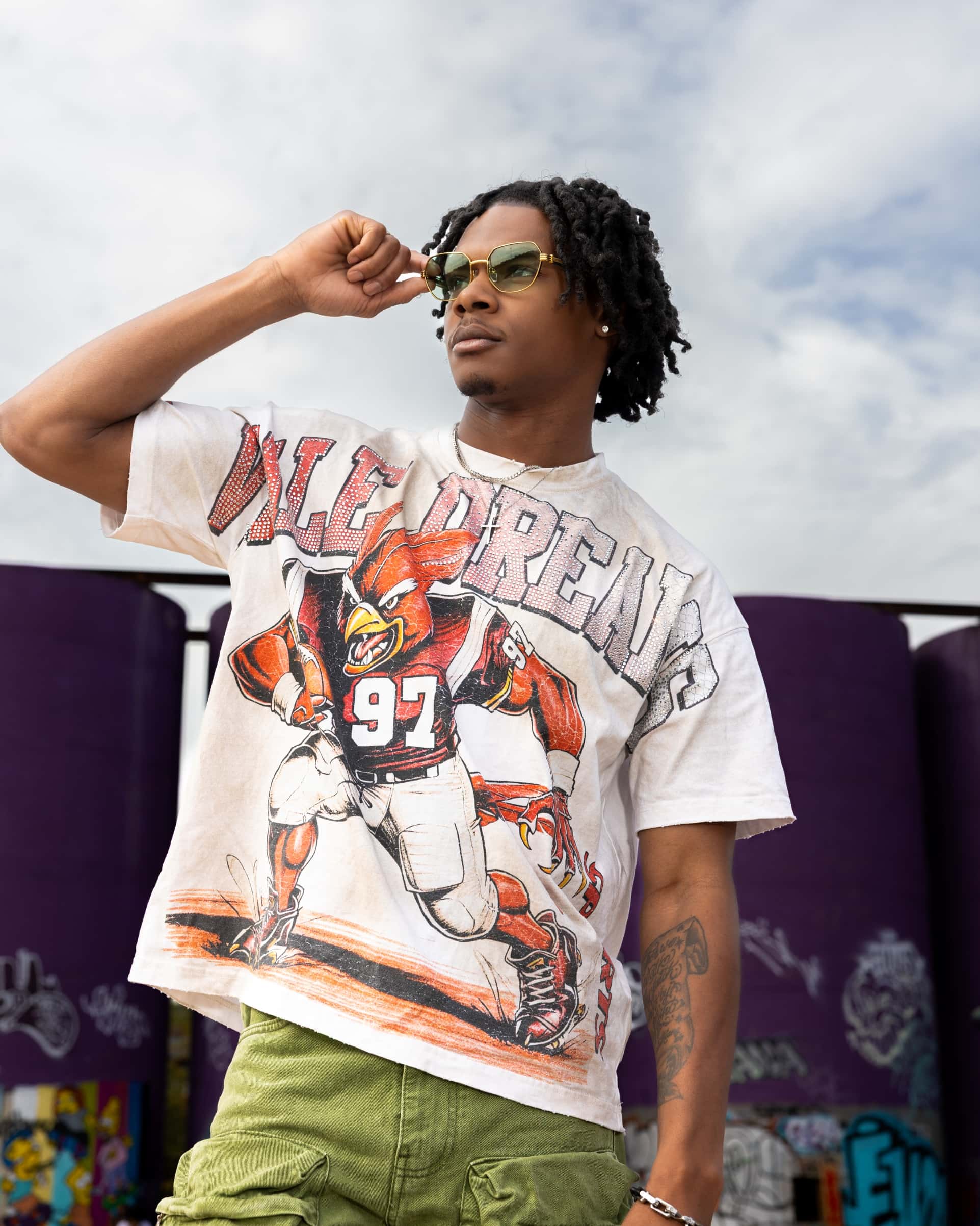 Person wearing a vintage football jersey with a graphic design against a graffiti-covered wall.