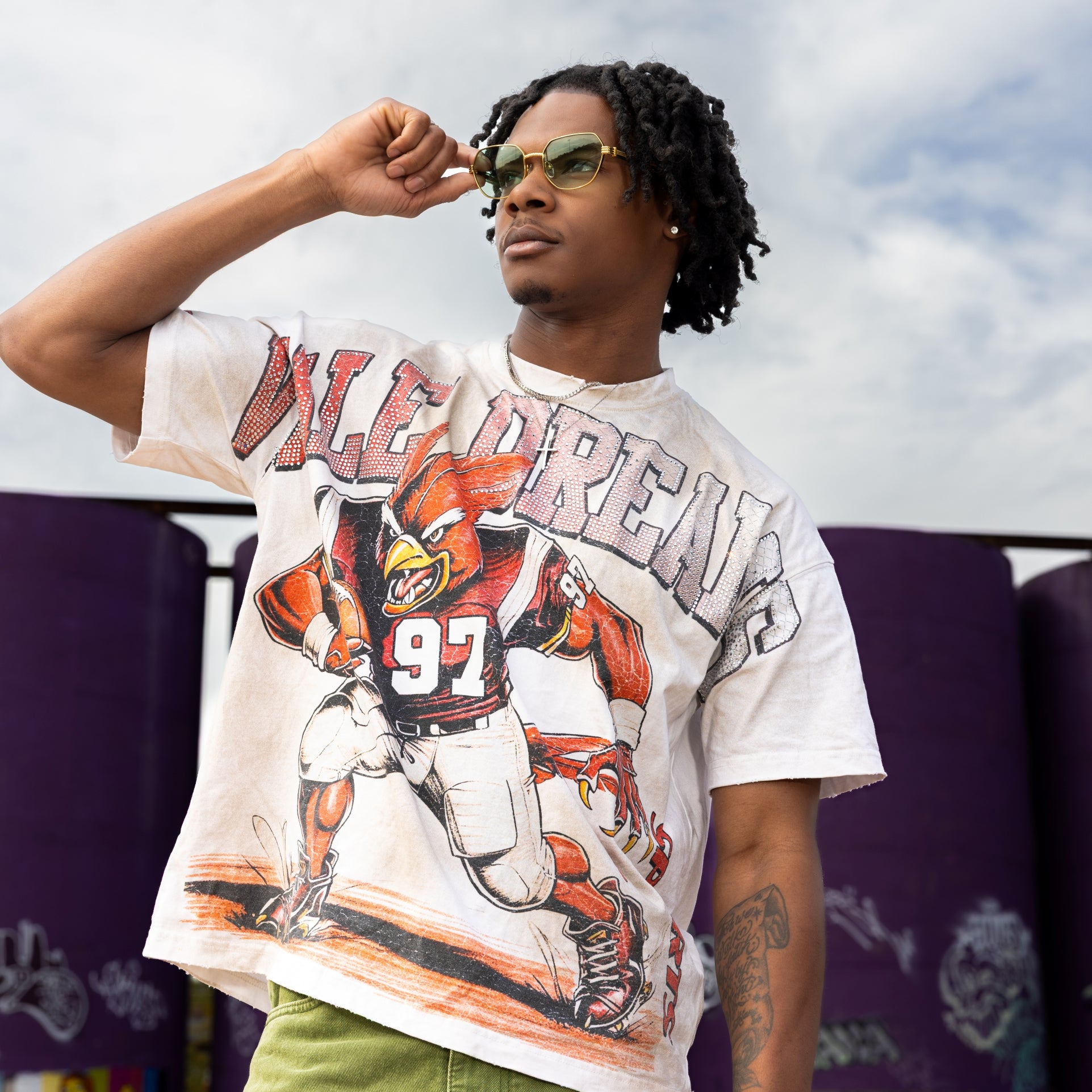Person wearing a vintage football jersey with a graphic design, standing outdoors against a graffiti-covered wall.