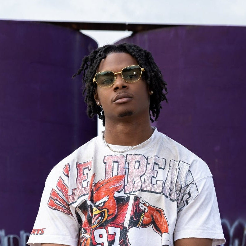 Person wearing a graphic t-shirt and green cargo pants standing in front of graffiti-covered walls.
