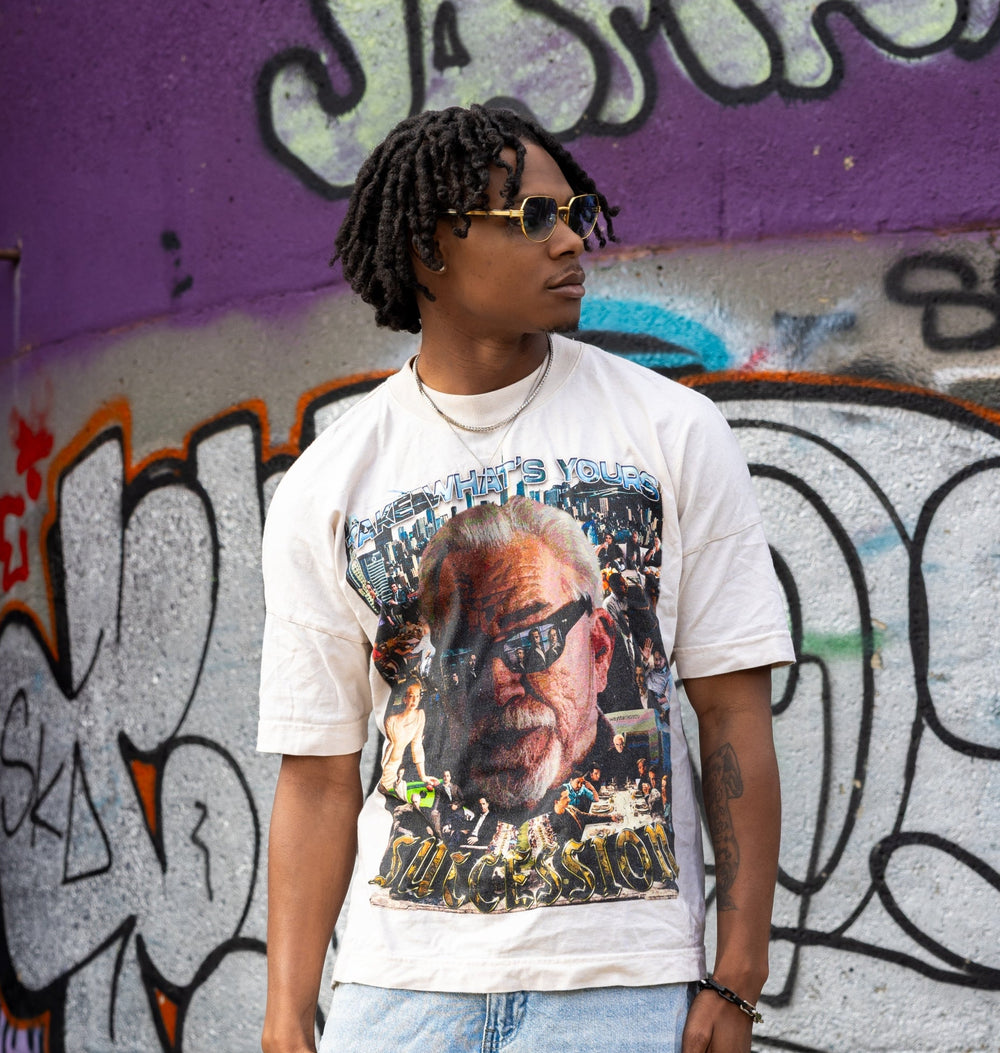 Person wearing a white t-shirt with a graphic design in front of a graffiti-covered wall.