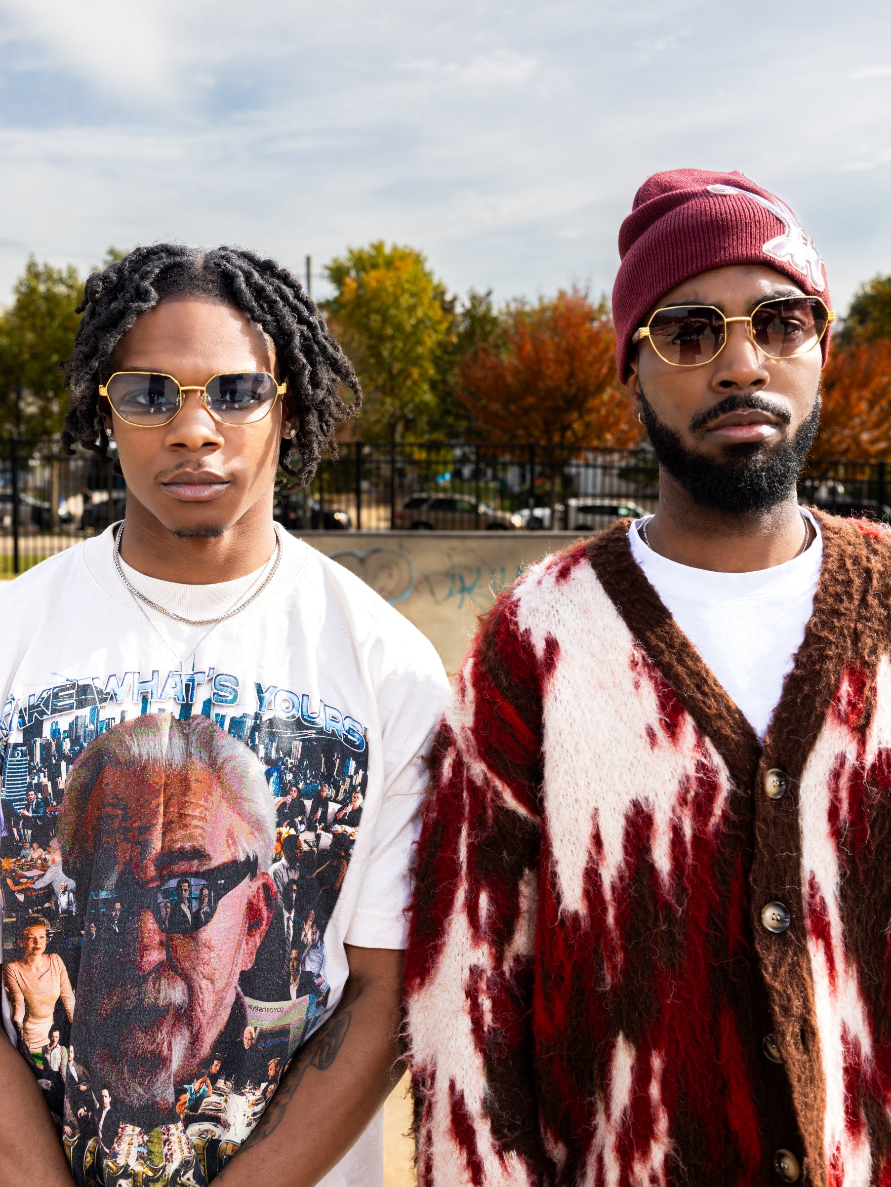 Two men standing outdoors with trees and a cloudy sky in the background