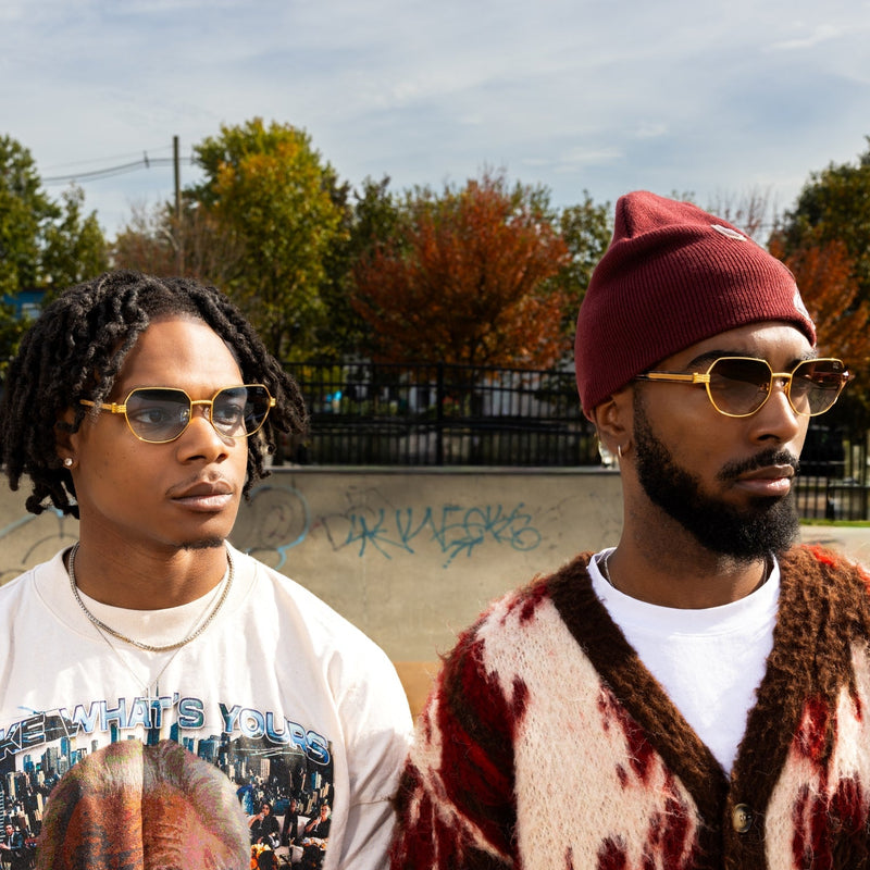 Two men standing outdoors with trees and a clear sky in the background