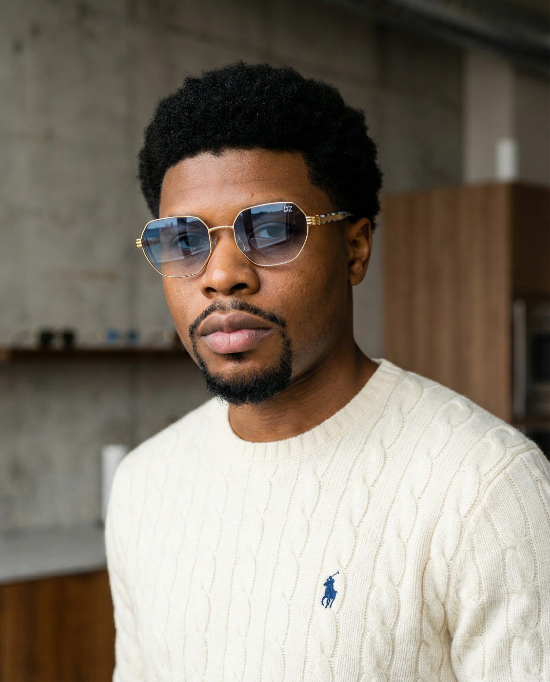 Man wearing sunglasses and a white sweater with a logo in an indoor setting