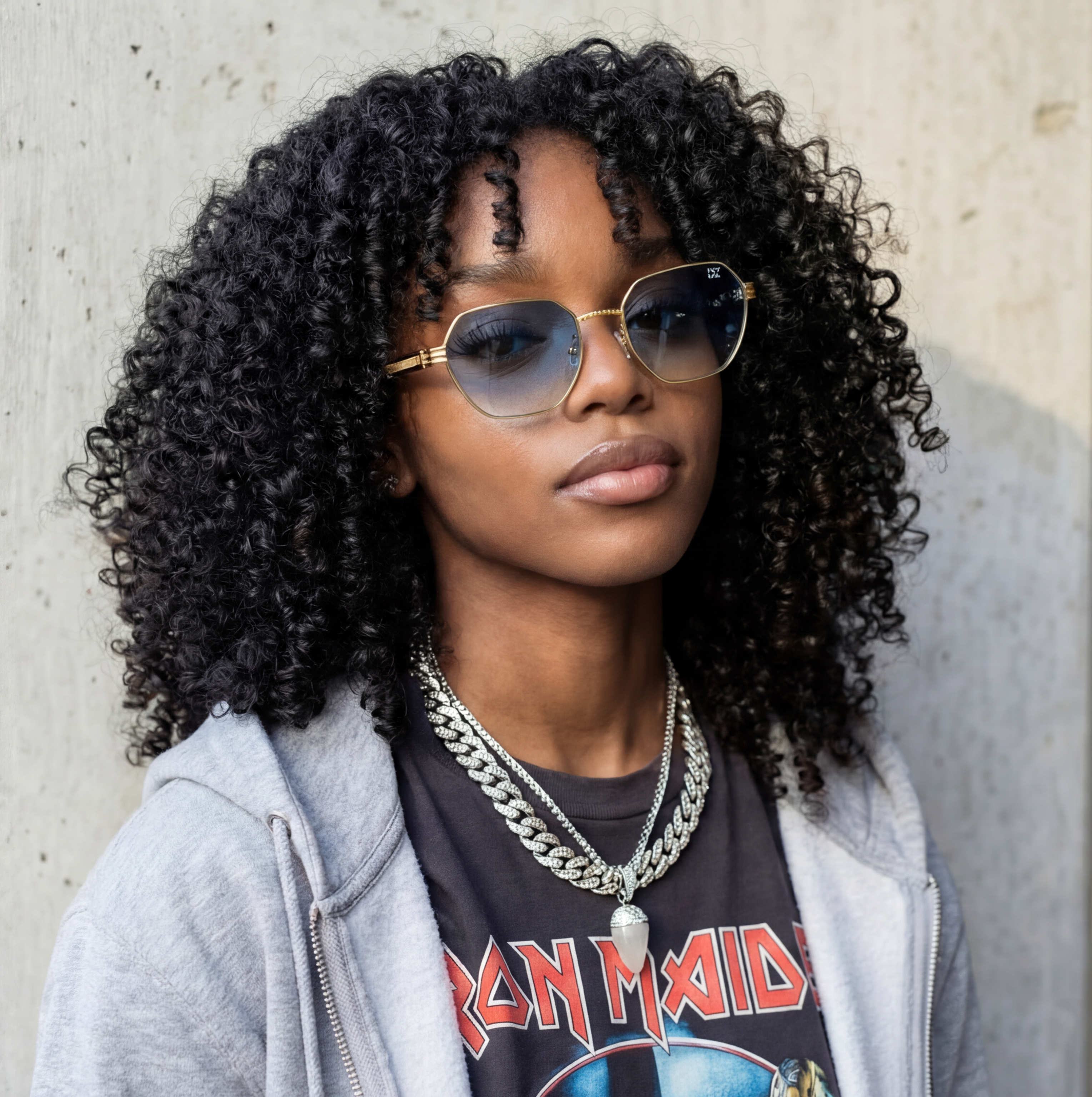 Person with curly hair wearing sunglasses and a graphic t-shirt against a concrete wall.