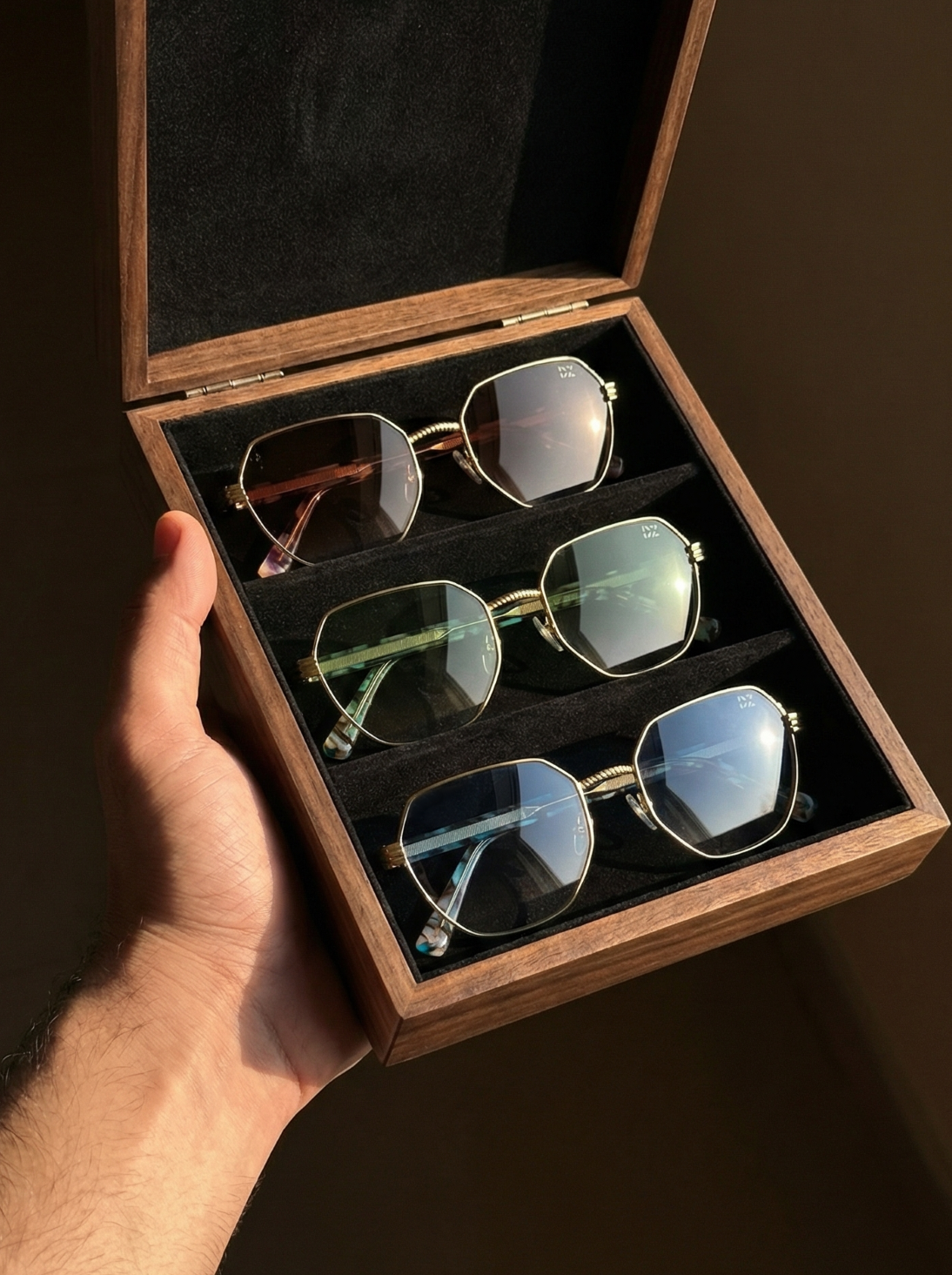 Hand holding a wooden box with four pairs of sunglasses inside.